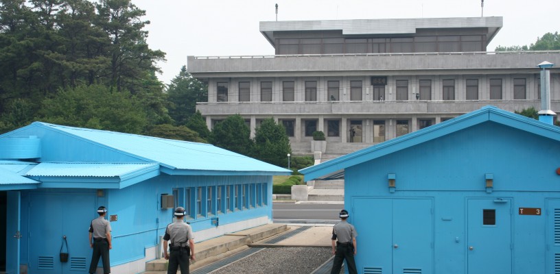 Conference Row at the Joint Security Area in Korea, seen from the South Side. The building in the background is Panmun House. The concrete line running through the huts is the MDL, the official border between the two countries. The ROK solders stand with half of their body obscured in order to provide a smaller target to those on the North, as well as to be able to signal unseen if necessary.